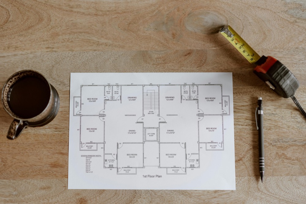 A floor plan with a tape measure and pencil on a wood workbench